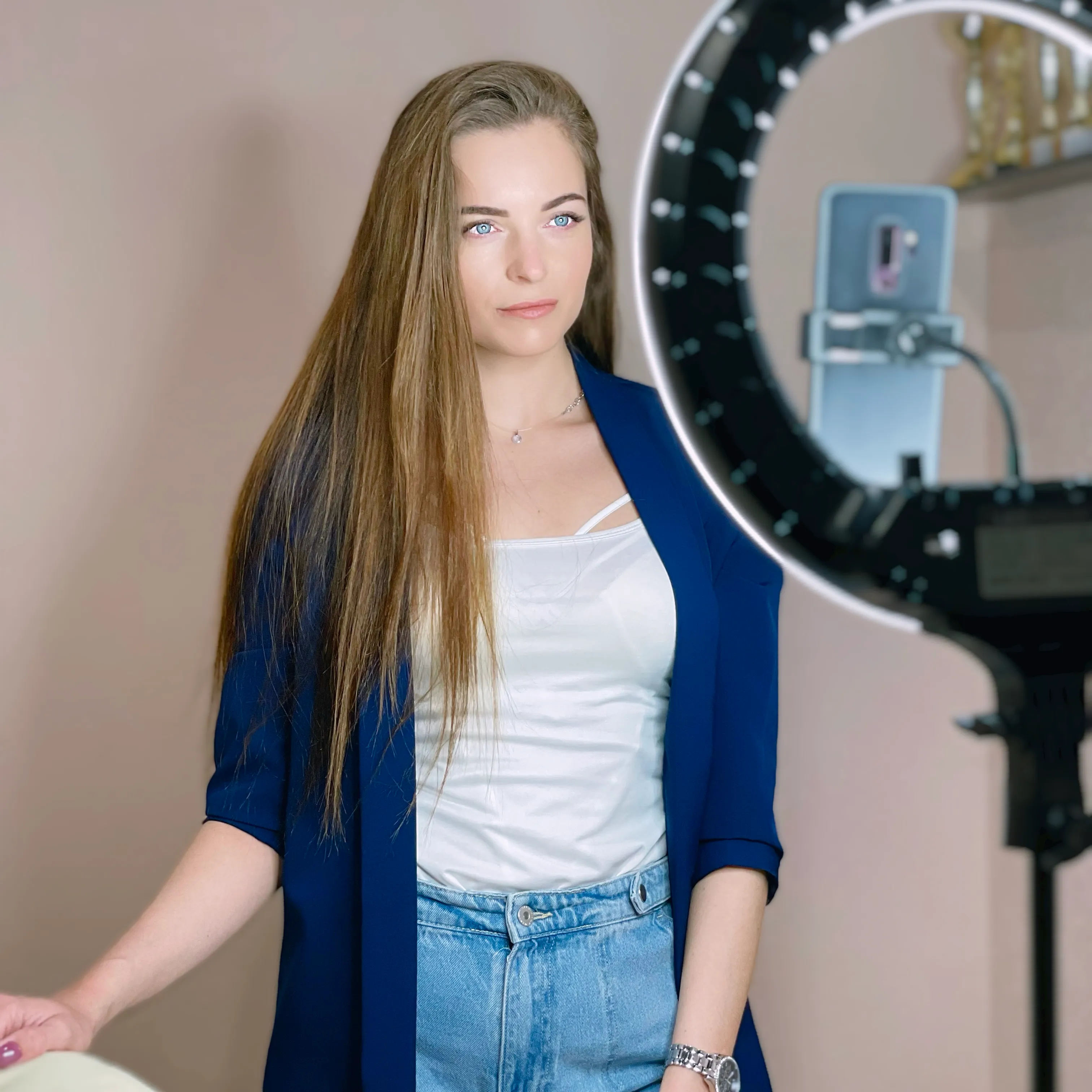 Woman in a blue blazer standing beside a ring light.